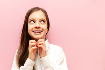 modest pensive teenage girl with braces thinks and imagines on a pink isolated background, the...