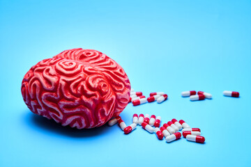 Representation of a red brain with a pile of red and white pills on a blue surface. Concept of addictions.
