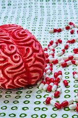 Brain of red human drug addict surrounded by red and white pills and capsules.