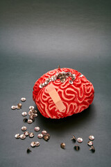 Close-up of a red rubber human brain with a bunch of thumbtacks on top of it against a dark background. Concept of extreme headache.