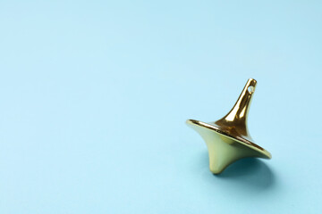 One golden spinning top on light blue background, closeup. Space for text