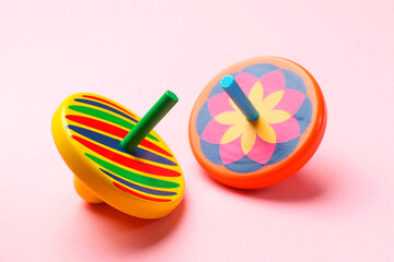 Two colorful spinning tops on pink background, closeup