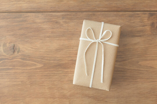 Present wrapped in kraft paper wrapping paper on wooden table seen from overhead	

