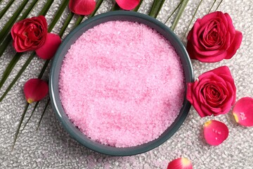 Natural sea salt in bowl, rose flowers and petals on grey textured table, flat lay