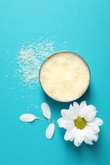 Natural sea salt in bowl, chamomile and petals on light blue background, flat lay