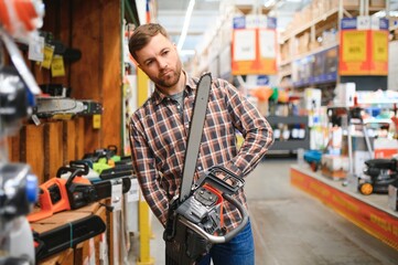young male is standing with new electric saw in tools store