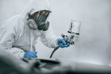 In protective mask and wear. Close up view of man that is painting a car by using spray guy