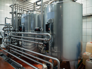 Modern brewery setup with large stainless steel fermentation tanks connected by sophisticated network of pipes. Brewing process, precise temperature control and sterilization.