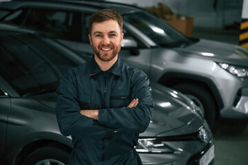 Repairman in uniform is standing in the garage with cars