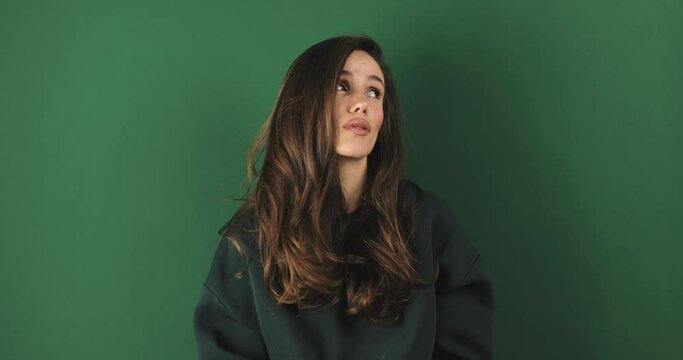 Brunette woman looking by side with sad expression over isolated green background. Break up and divorce, difficult period of life. Mental health. Girl wear green pullover.