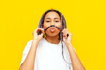 young african american woman with dreadlocks shows a mustache from her hair on a yellow isolated...