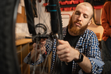 Bearded redhead male mechanic repairing a bicycle in a garage or workshop.