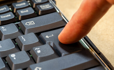Man pressing an enter key on a laptop computer keyboard, finger pushing the key object detail closeup, one person. Accepting, confirming an action, sending a chat message simple abstract concept