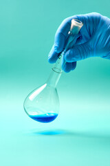 Hand of unrecognizable researcher in latex glove holding titration flask of blue chemical substance during experiment in laboratory