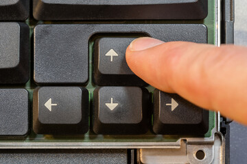 Man pressing the up arrow key on a simple laptop computer keyboard, top down table top view from above. Finger presses the forward arrow, moving forwards, progress simple abstract concept, one person