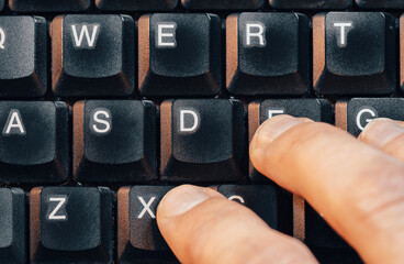 Mans hand resting on an old retro style aesthetic laptop computer keyboard with thick keys, top view shot from above, one person. Retro computing, typing writing inputting text simple abstract concept