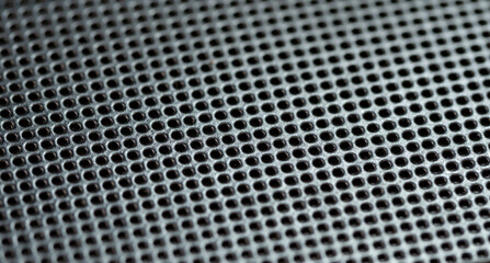 Close-up shot of a detailed perforated metal surface background texture, pattern of small, uniform holes with a selective focus, shallow depth of field. Strong material shiny steel backdrop, nobody