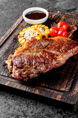 Delicious grilled steak with roasted corn, fresh tomatoes, and sauce, served on a rustic wooden board. Perfect for a hearty meal