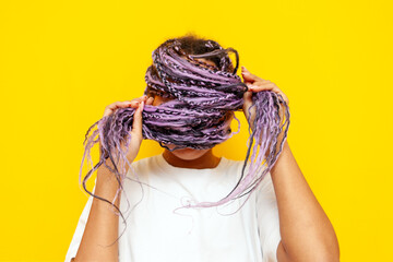 young african american woman with dreadlocks covers her face with her hair and hides on a yellow...