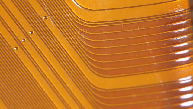 A detailed close-up of a copper colored flexible flat ribbon cable with parallel conductive lines, warm orange abstract technology background texture with copy space, nobody, macro detail closeup