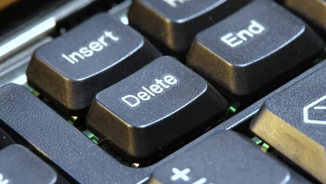 Finger pressing the Delete key on a simple laptop computer keyboard, object macro detail, extreme closeup. Deleting files, removing content, digital data deletion abstract concept symbol, one person