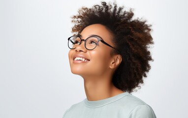 Fototapeta premium Young woman with curly hair and glasses looking up with a joyful expression, on a light background