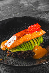 Grilled salmon fillet on avocado slices, garnished with red caviar, served on quinoa in a dark bowl. A vibrant, gourmet dish indicative of fine dining