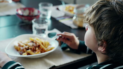 Back of child eating pasta at lunch table. Family lifestyle scene of young boy enjoying carb-rich...