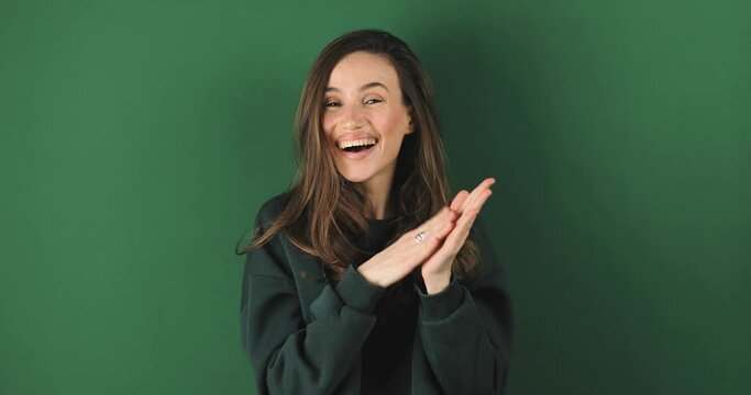 Young woman applauding after presentation in a conference isolated on green background. Applauding girl is very glad and happy, she claps hands because of excellent news, support, wow emotions.
