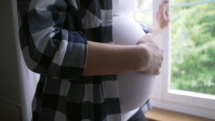 Close-up of mother caressing belly, expecting newborn child - 8 month pregnancy by residence window