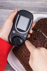 Hand of child holding glucose meter, sweet chocolate cake. Checking sugar level during diabetes
