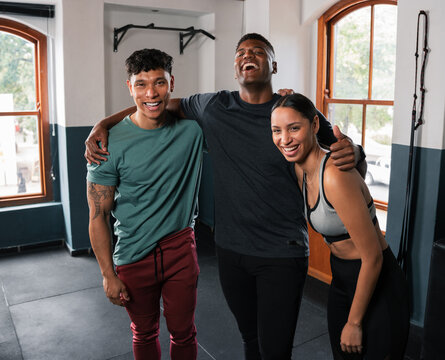 Two women and a man smiling in gym, showing shoulders and muscle in leisure wear
