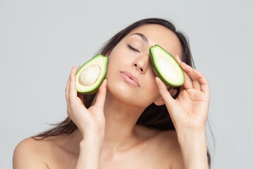 Young beautiful brunette with closed eyes holding two avocado halves in her hands