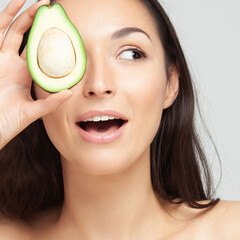 An avocado cut into two pieces in hands of young playful woman
