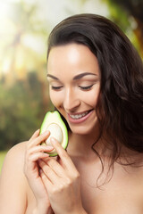 Half an avocado in hands of young laughing woman against forest background