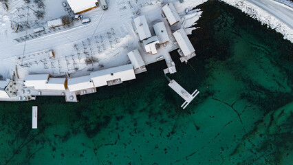 Sakrisoy auf den Lofoten von oben, Drohnenaufnahme zeigt schneebedeckte Dächer und tieftürkises...