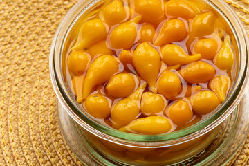 Pickled whole Biquinho Yellow chili in a glass jar on a yellow background. Sour and sweet Asian-style pickled homegrown chilies.