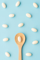 White soft gelatin capsules with wooden spoon on light blue background. Concept of probiotic supplement, vitamins and painkiller addiction.