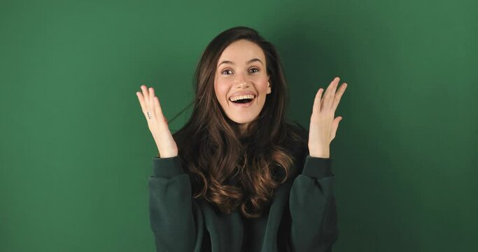 Happy woman looking camera shocked surprised say wow cover mouth, spread hands. Wow, it is awesome. Surprised girl face. Close up of shocked woman face expression isolated on green background.