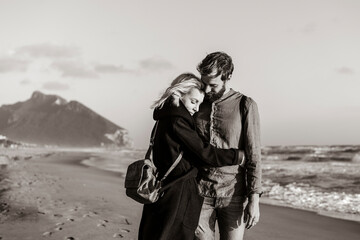 A couple finds solace in each other's arms amidst the tranquility of the sea. Monochrome intimacy on a secluded beach.