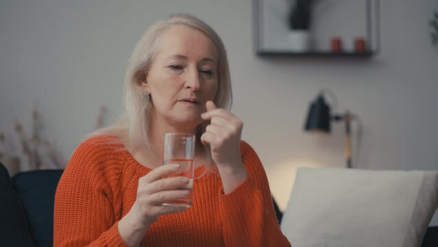 Middle-aged woman taking pills with water, hormonal therapy, disease treatment