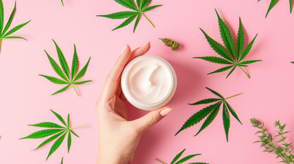 A woman's hand demonstrates a jar of cream on a pink background highlighted by fresh cannabis leaves and buds - obrazy, fototapety, plakaty
