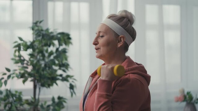 Athletic woman in her 50s lifting dumbbells at home, active lifestyle, wellbeing