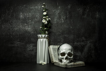 A creepy still life with a white skull on an open book next to a vase of flowers