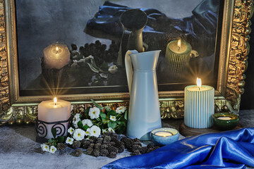 A still life with a blue satin fabric next to several lit candles, flowers and their reflection on a black surface