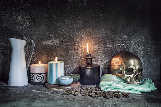 A still life with a golden skull on a green satin cloth next to several lit candles