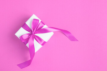 Gift box with tied pink bow on the pink background. Top view. Copy space.
