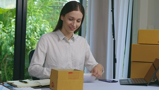 Woman packing parcel box. Business owner work at home wrapping parcel box. Woman prepare parcel box of product for deliver to customer in her home office. Online sales and Parcel shipping.