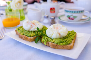 Perfectly poached organic eggs on avocado toast served for breakfast with tea and orange juice
