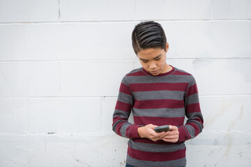 Fashionable teenage asian boy standing alone against a white background using his smartphone.